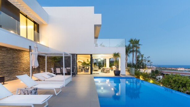 Ein modernes Haus mit Swimmingpool, Sitzgelegenheit im Freien und Meerblick.