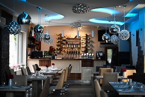 A restaurant with a bar area, tables set for dining, and hanging spherical light fixtures. - Fenyves Konferencia és Wellness Hotel (Baktalórántháza)