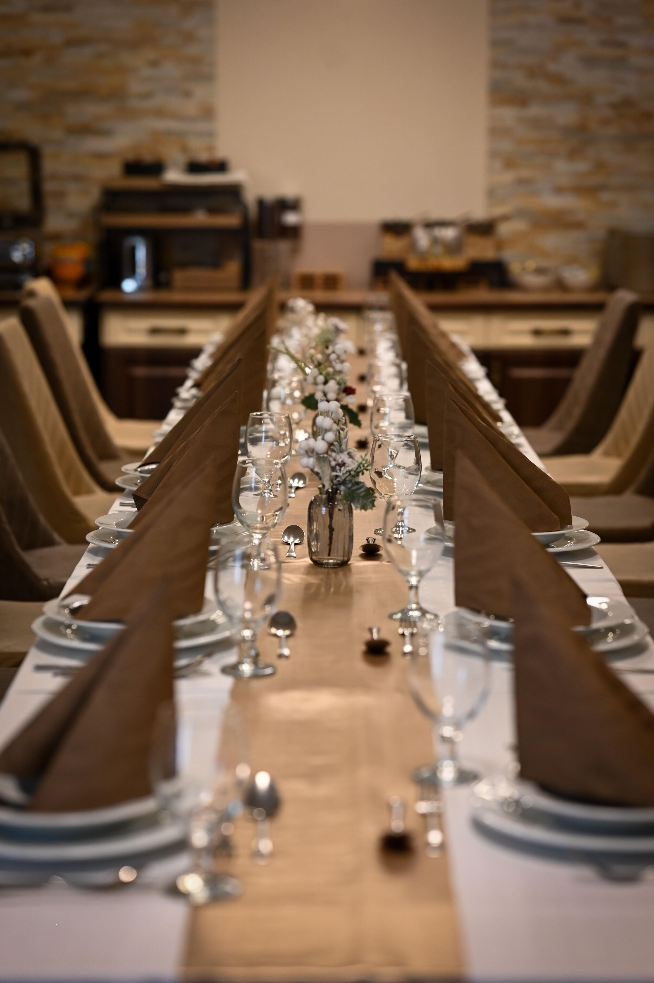 A long dining table set with multiple chairs, a vase with flowers, and a wooden table runner.