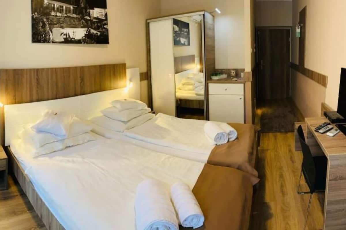 A hotel room with a bed, a desk with a television, a mirror, and a wardrobe.