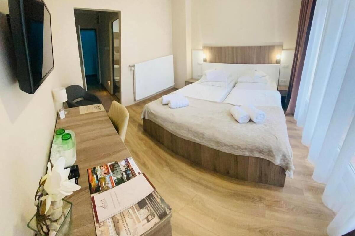 A hotel room with a bed, a desk, a chair, a TV, and an air conditioning unit.