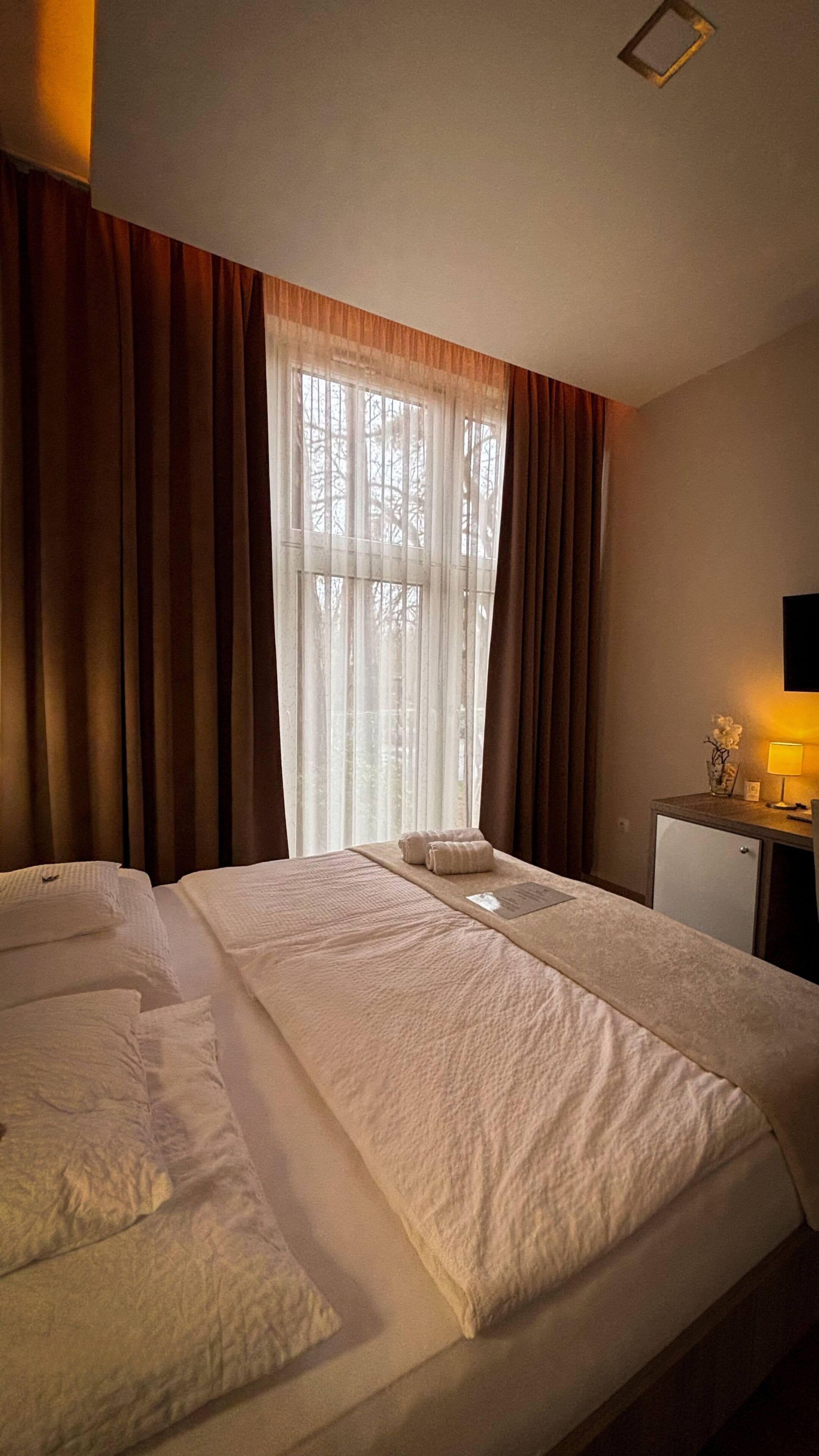 A hotel room with a large bed, a desk with a lamp, and a window with curtains.