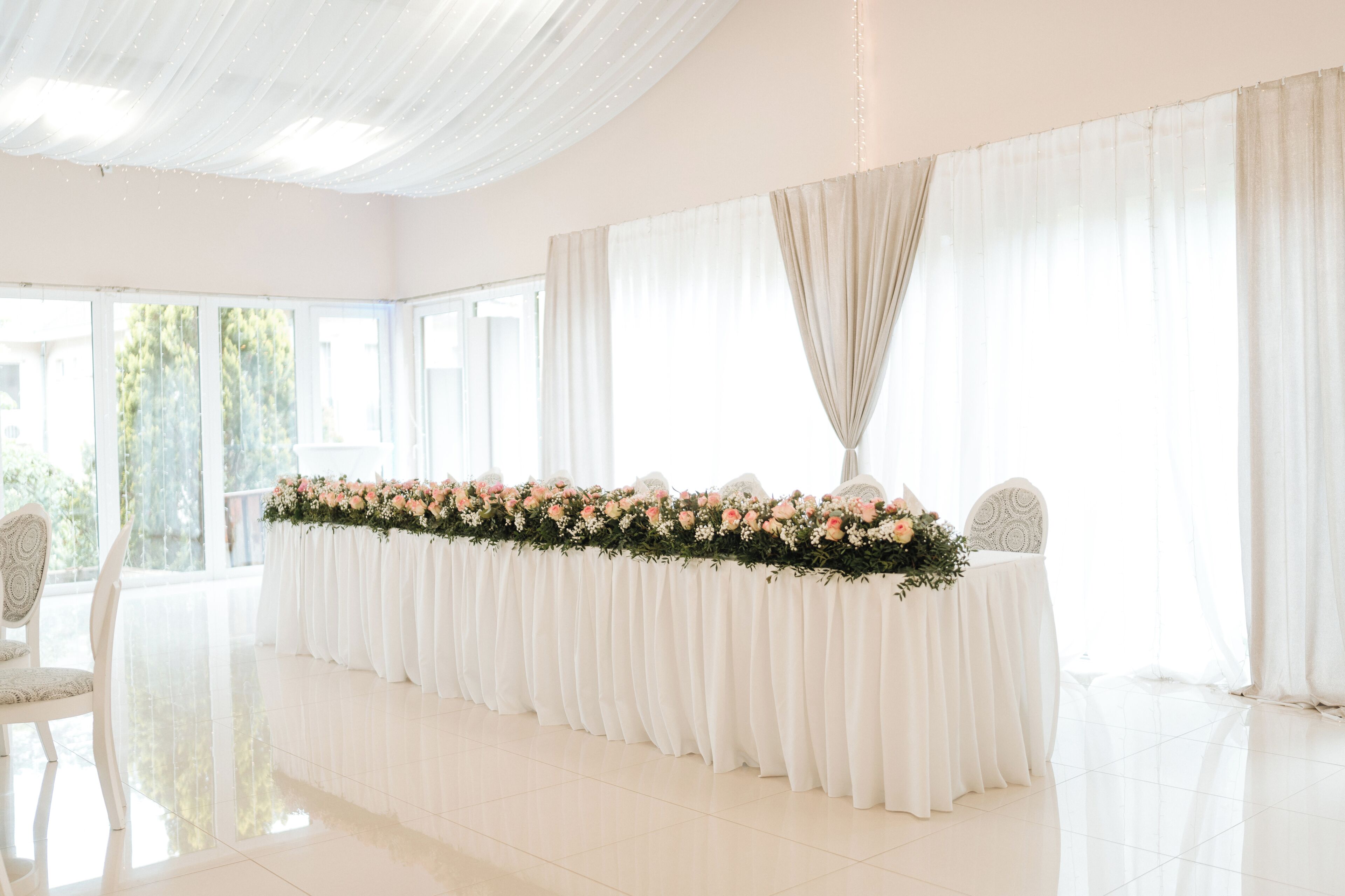 Amplia habitación con una larga mesa decorada con flores, ventanas grandes y un techo alto.