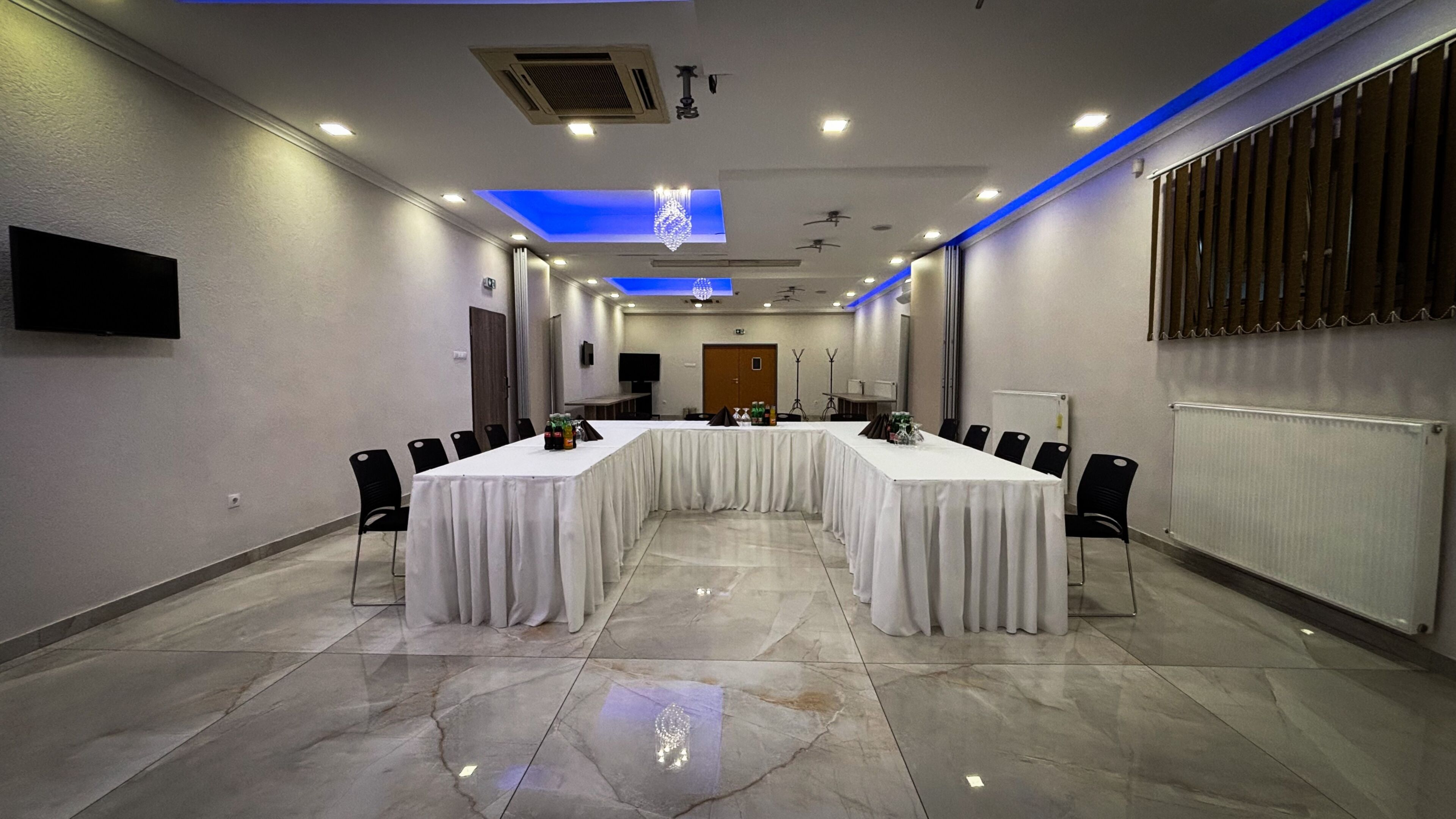 A conference room with a long table, chairs, a flat-screen TV, and a ceiling light.