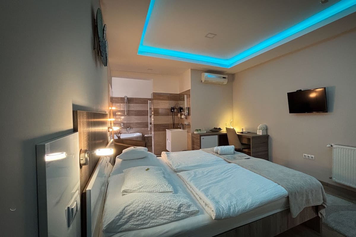 A hotel room with a bed, bedside table, desk, chair, TV, and a bathroom with a shower and sink.