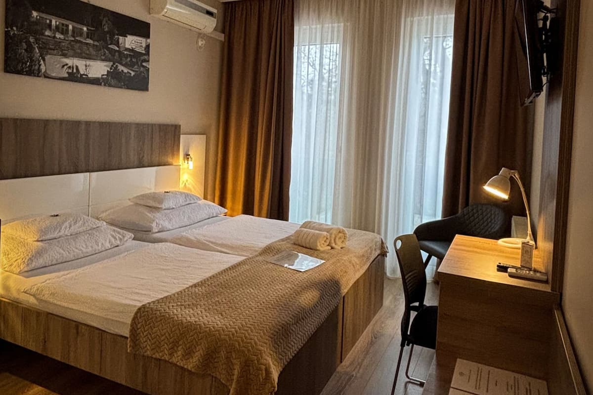 A hotel room with a large bed, a desk, a chair, a flat-screen TV, and an air conditioning unit.