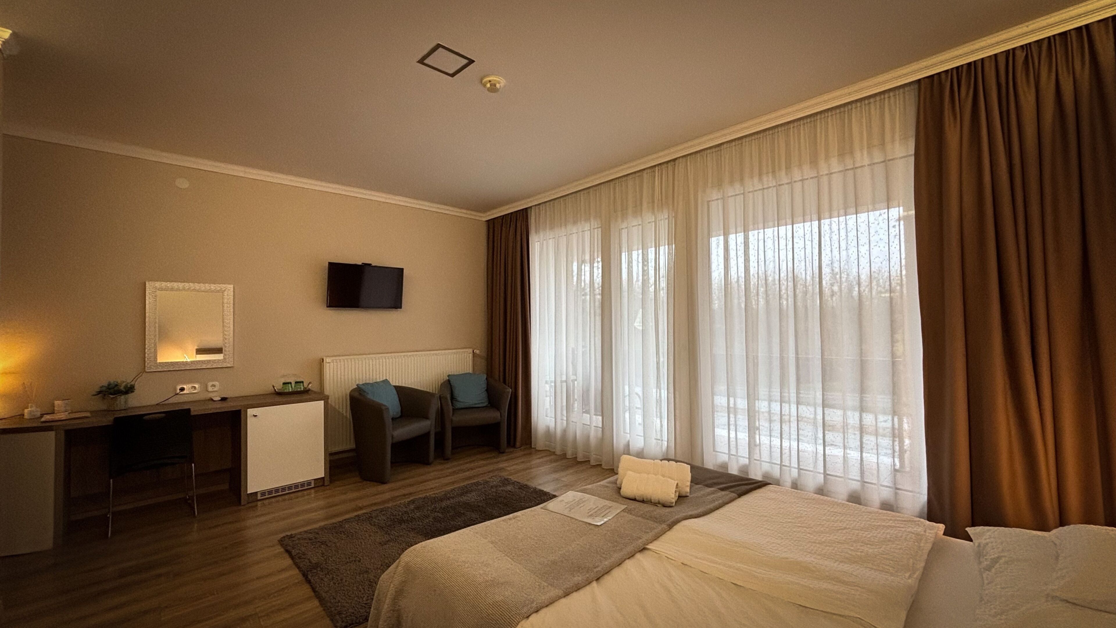 Habitació d'hotel amb llit, escriptori, cadira, televisió i finestra amb cortines.