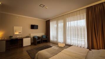 Habitació d'hotel amb llit, escriptori, cadira, televisió i finestra amb cortines.