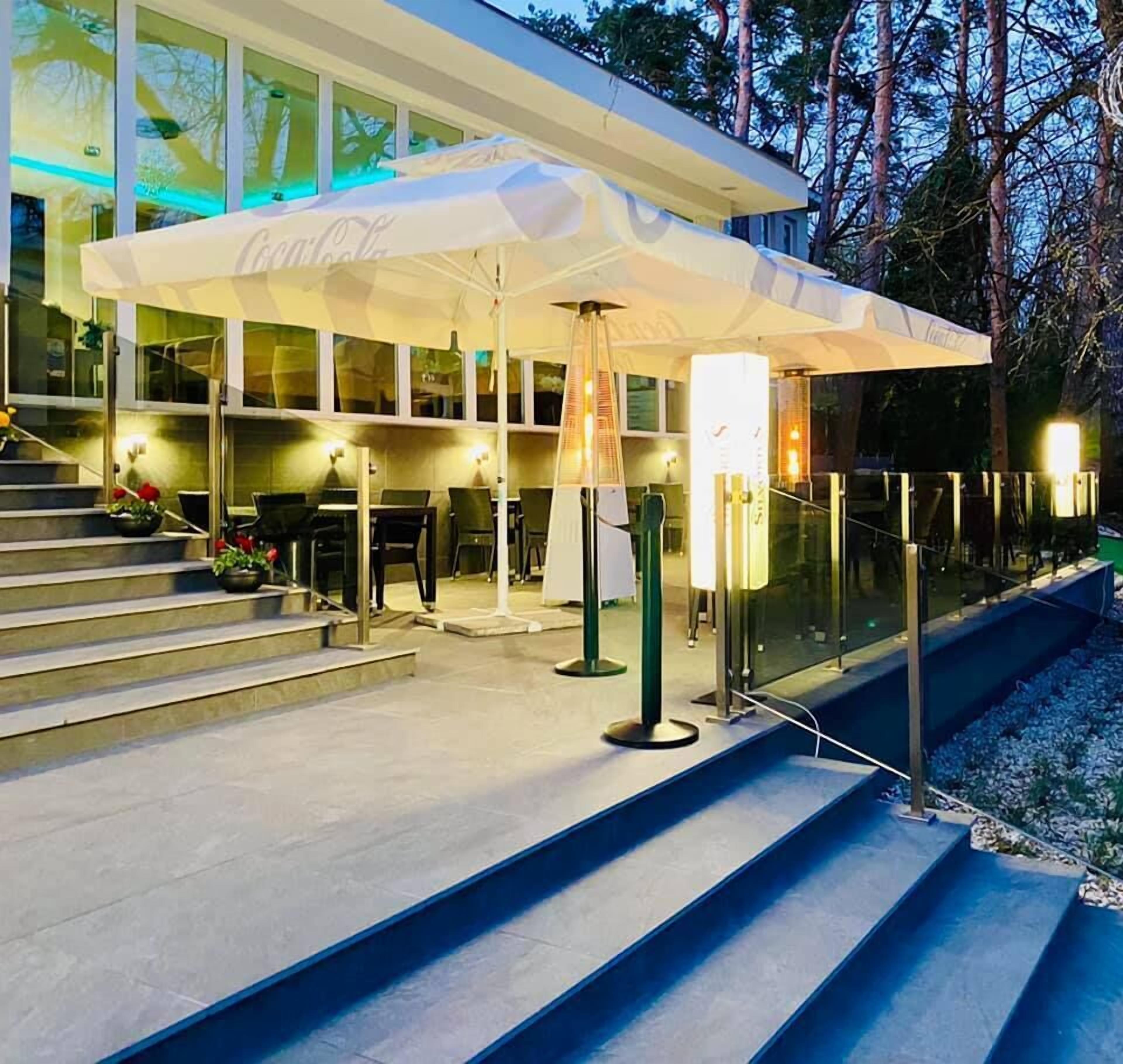 Un edificio moderno con un área de estar al aire libre con la marca Coca-Cola, escalones que conducen a la entrada y una barandilla de vidrio.