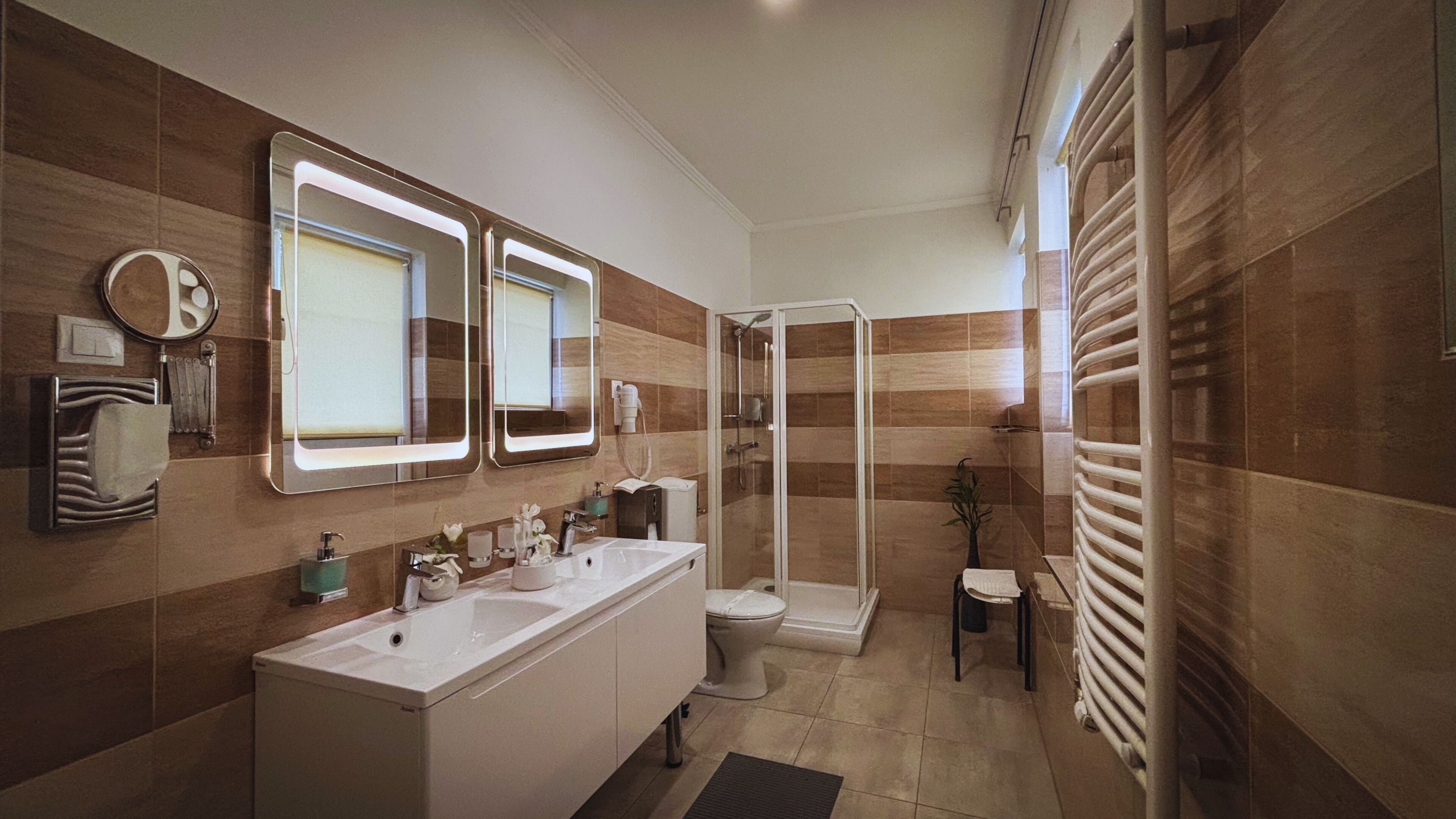 A modern bathroom with a shower, two sinks, a toilet, and a towel rack.