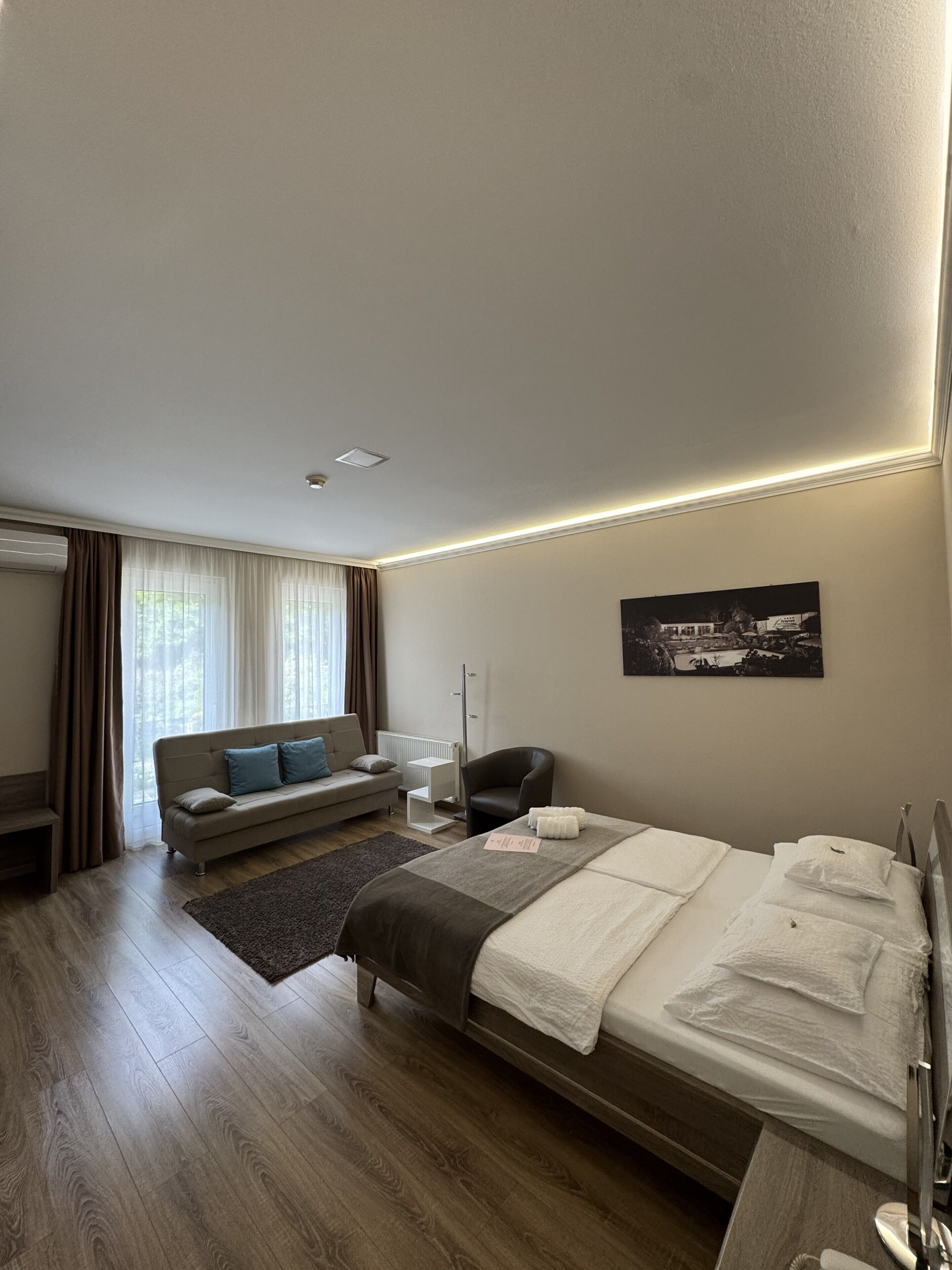 Ett hotellrum med en säng, en soffa, en stol, ett skrivbord och ett fönster med gardiner.