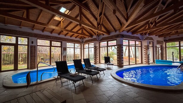 Una piscina interior con techo de madera, paredes de piedra y ventanas amplias.