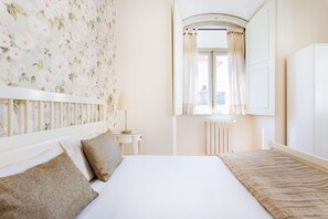 Une chambre d’hôtel avec un grand lit, une petite table, un miroir et une fenêtre avec des rideaux.