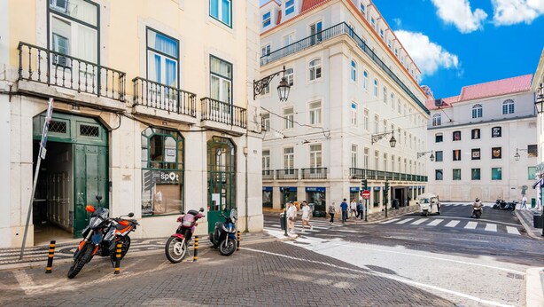Straßenansicht mit Gebäuden, einer Zebrastreifen und abgestellten Motorrädern.