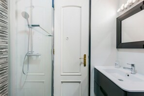 Une salle de bain moderne avec une douche à parois de verre, une porte blanche et un lavabo avec un miroir au-dessus.