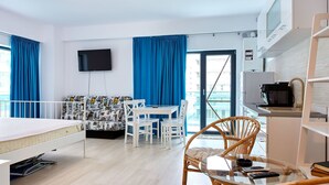 Habitación de hotel moderna con una cama, un área de comedor con mesa y sillas, un televisor montado en la pared y un balcón con vistas.