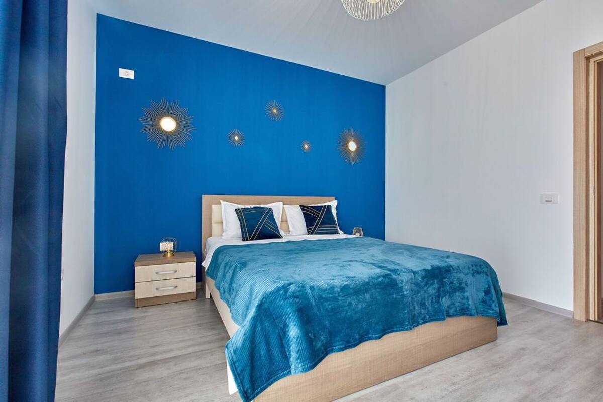 Quarto com parede azul de destaque, estrutura de cama de madeira e mesa de cabeceira com gavetas.