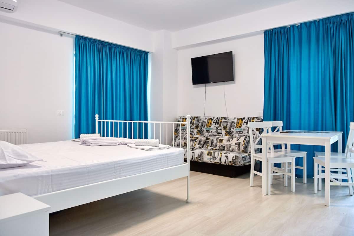 Quarto de hotel com cama, escrivaninha e uma cadeira. Há uma televisão presa à parede.