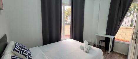A hotel room with a bed, a desk, and a window with curtains.
