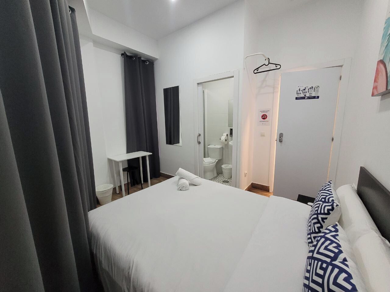 Una camera d'albergo con un letto, una scrivania e un bagno visibile attraverso una porta aperta.