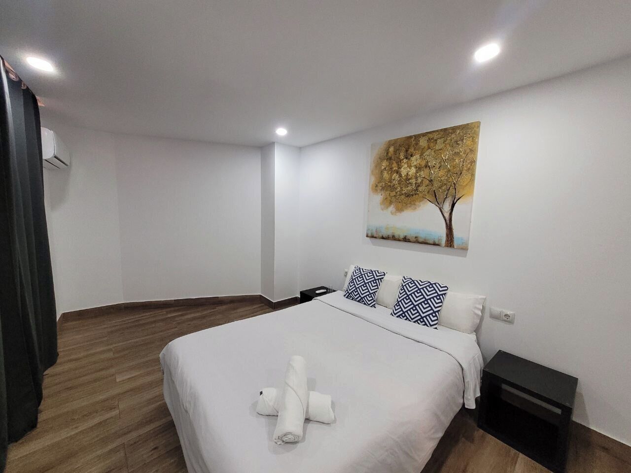 A neatly arranged bedroom with a bed, pillows, a nightstand, and a painting on the wall.
