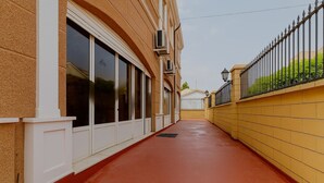Un pasillo con suelo rojo, marcos de puerta blancos y una pared amarilla con una cerca de metal negro.