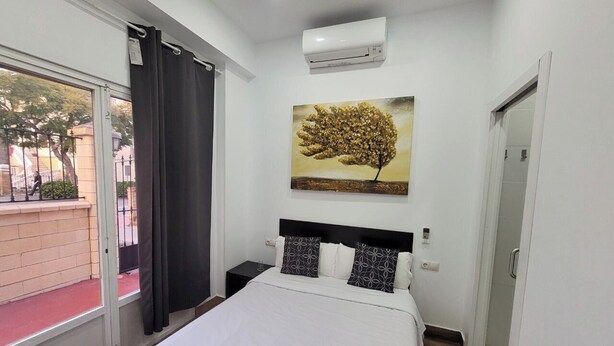 Habitación de hotel con cama, un cuadro, aire acondicionado, ventana con cortinas y vistas al exterior.