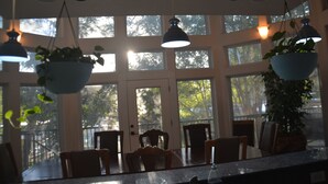 A dining area with a large window, hanging plants, and a table set for four. - Large Mediterranean pool, river, basketball, sleeps 26, 8 bedrooms (seguin)