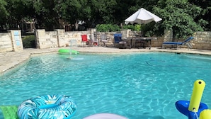 A clear swimming pool with inflatable toys, stone walls, and a stone bench area. - Large Mediterranean pool, river, basketball, sleeps 26, 8 bedrooms (seguin)