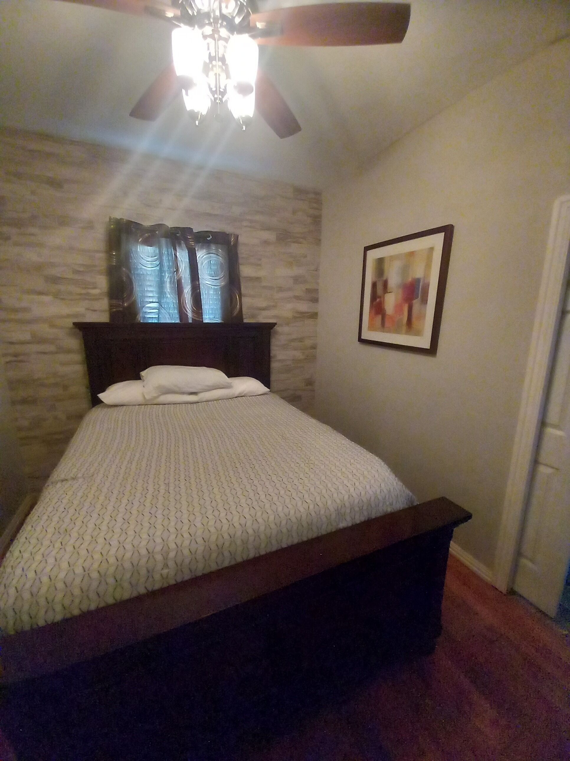 A bedroom with a bed, a ceiling fan, a window with curtains, and a framed picture on the wall.