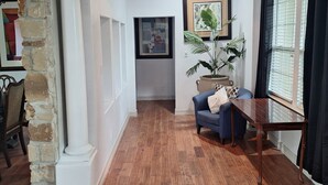 A hallway with wooden flooring, a dining area with a table and chairs, a chandelier, and a potted plant.