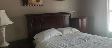 Un dormitorio con cabecera de madera, colcha blanca y dos cuadros abstractos en la pared.