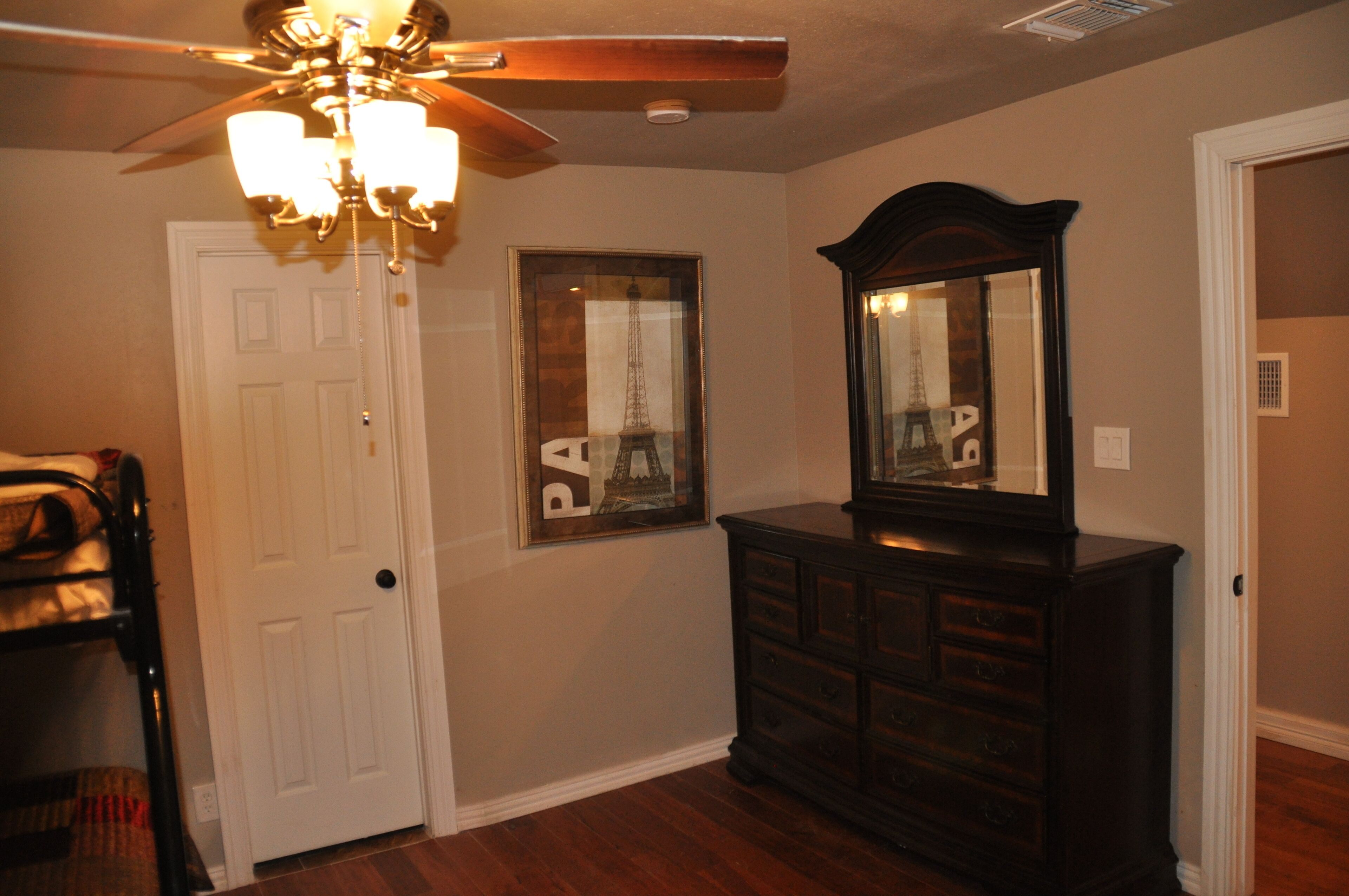 A room with a ceiling fan, a dresser, a door, and a framed picture of the Eiffel Tower.