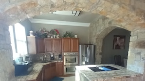 A kitchen with stone walls, wooden cabinets, a central island, and built-in appliances.