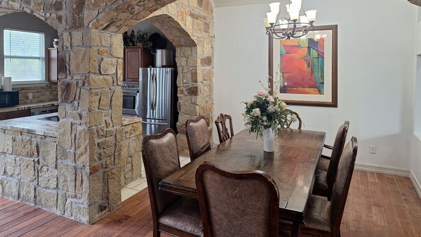 A dining area with a stone archway, a chandelier, and a painting on the wall.