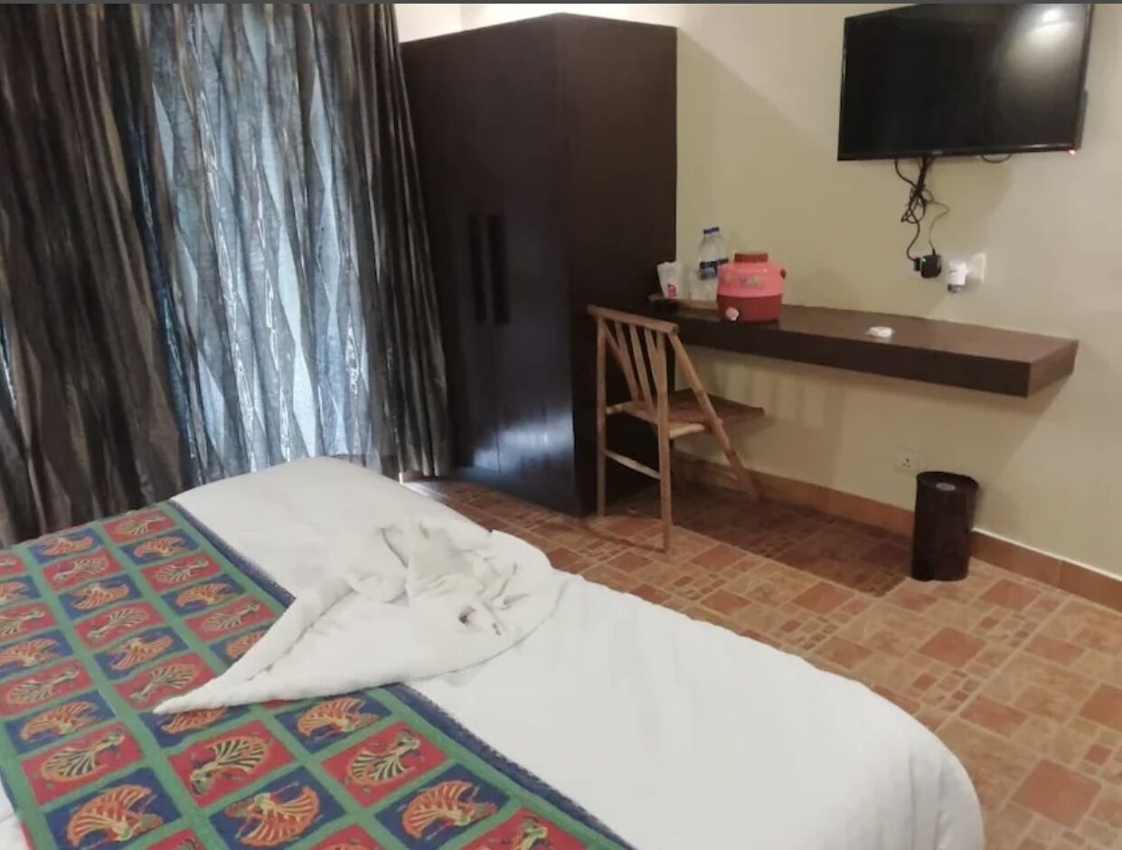 A hotel room with a bed, a desk, a chair, a TV, and a trash bin.