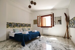 Relax in this serene bedroom with a large bed, marble floor, and a large window with wooden shutters.
