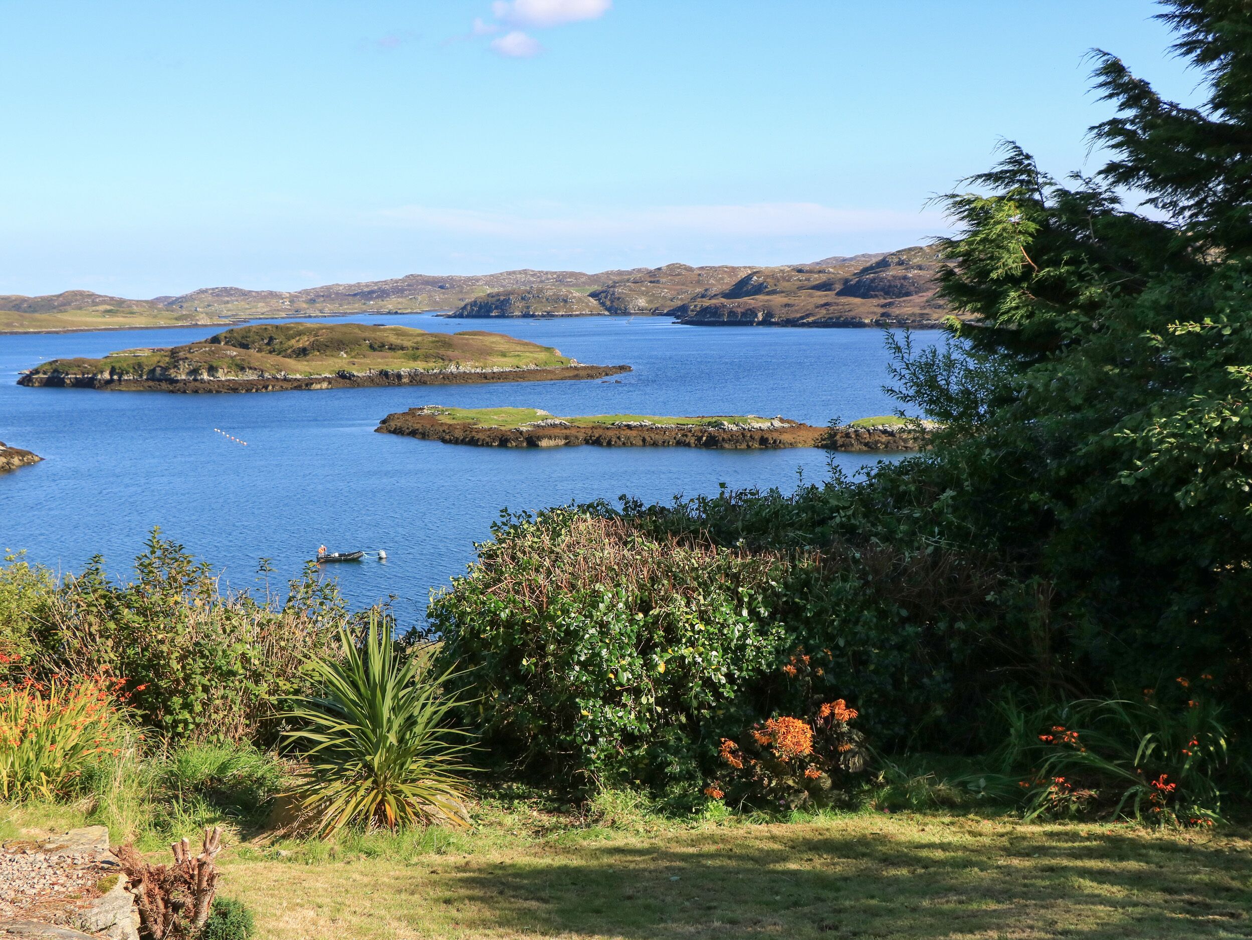 A coastal landscape with a clear view of a bay, several small islands, and lush greenery.