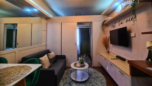 A modern living room with a sofa, a coffee table, and a TV mounted on the wall. There is a small plant on the coffee table and a decorative item on the wall. - One Bedroom Balcony With Great Location and Value (Makati)