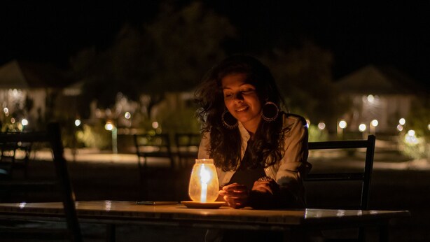 A person sitting at a table with a lit candle in a dimly lit outdoor setting. - Marvin Desert Camp (Jaisalmer)