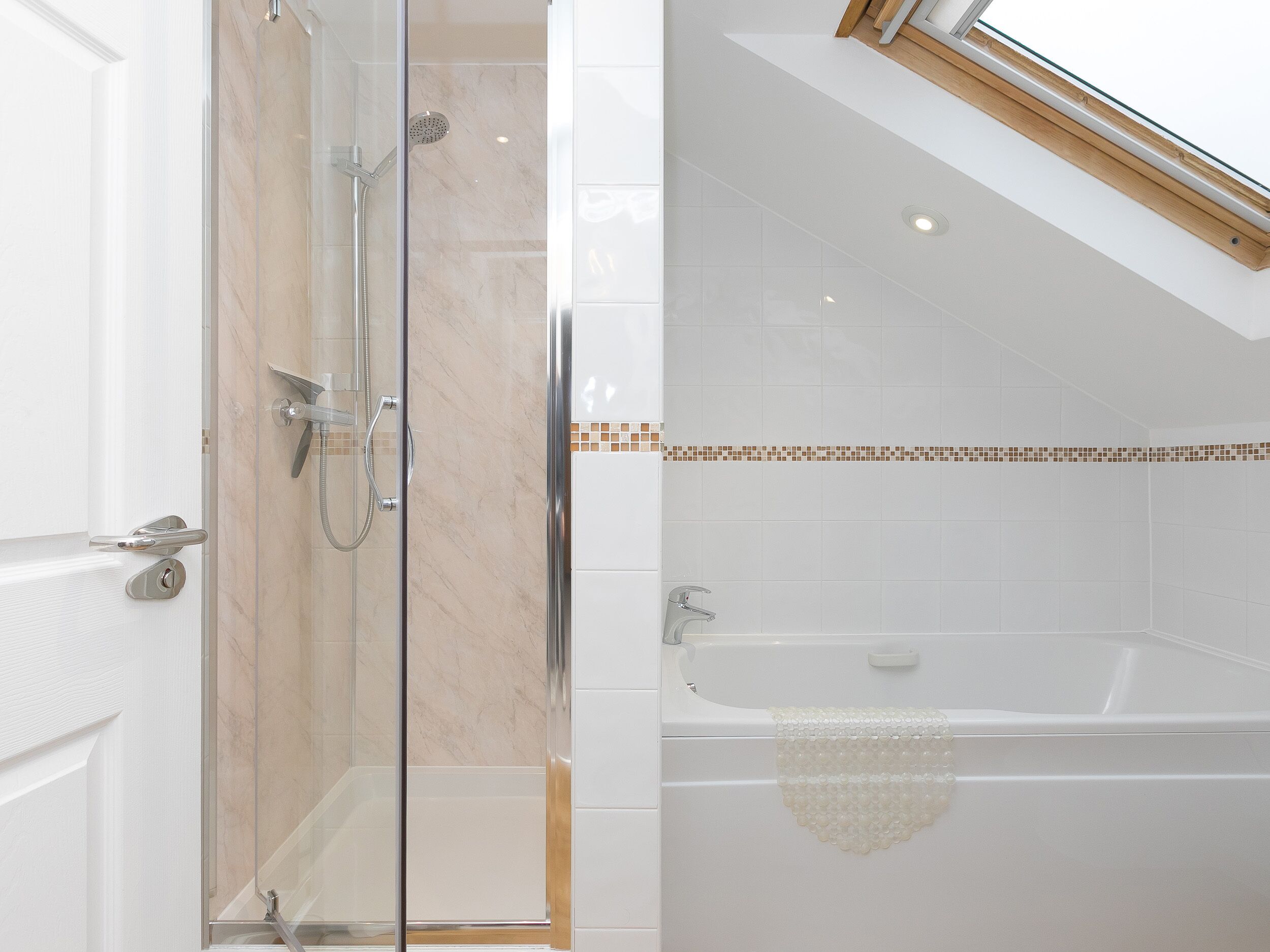 Ein modernes Badezimmer mit einer glasumrandeten Dusche, einer Badewanne mit einem beigefarbenen Handtuch und einem Oberlicht.