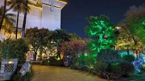 Un edificio moderno con una entrada bien iluminada, rodeado de jardines ajardinados y árboles.