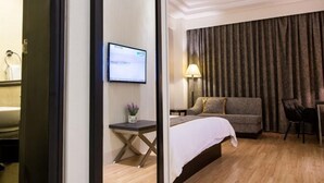 Una habitación de hotel con cama, escritorio, silla, televisor y cortina.