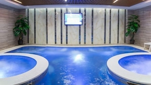 Una piscina interior moderna con dos jacuzzis, una pantalla digital y plantas en macetas.