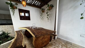 A rustic wooden table with a unique curved design, accompanied by two chairs. The setting includes a stone floor and potted plants on the walls. - Casa Moneda 5br old City AC Picusi (Bolívar)