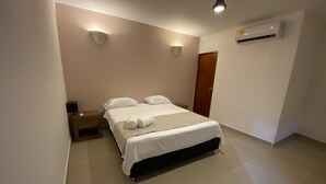 A neatly made bed with white linens and a rolled towel, a bedside table with a lamp, and a wall-mounted air conditioner. - Casa Moneda 5br old City AC Picusi (Bolívar)