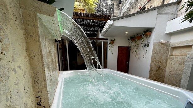 A hot tub with a waterfall feature, surrounded by stone walls and potted plants. - Casa Moneda 5br old City AC Picusi (Bolívar)