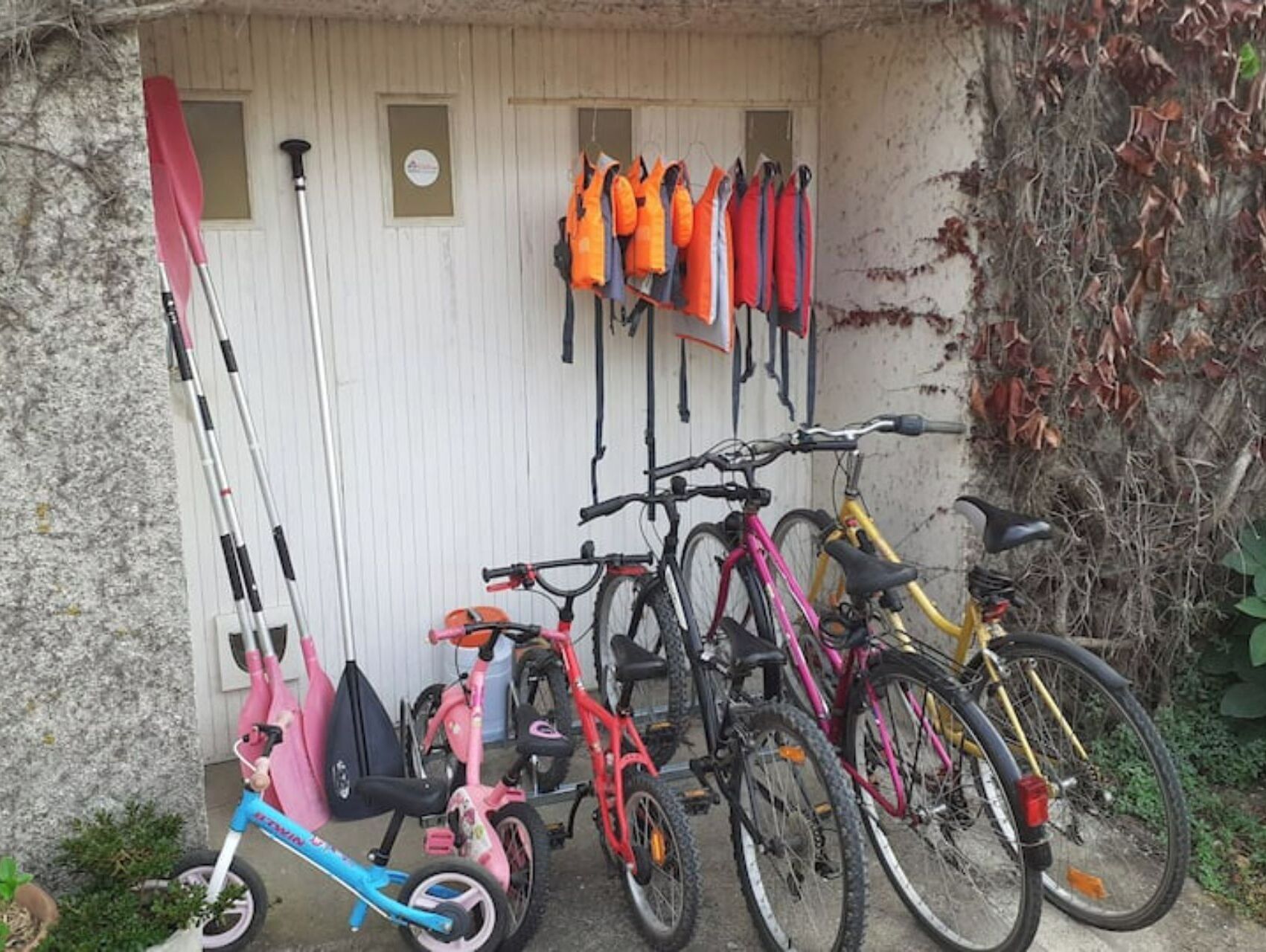 Een rij fietsen en een roze kinderfiets staan geparkeerd voor een gebouw met een witte gevel.