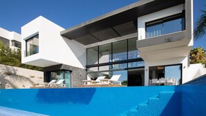 Une maison moderne dotée d’une piscine, avec une façade en verre et un toit plat.