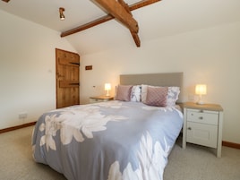 Un dormitorio con una cama, dos mesitas de noche, una puerta de madera y un techo inclinado con vigas a la vista.